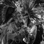 Black and white photo of performers in traditional indigenous attire during a parade in Mexico City.