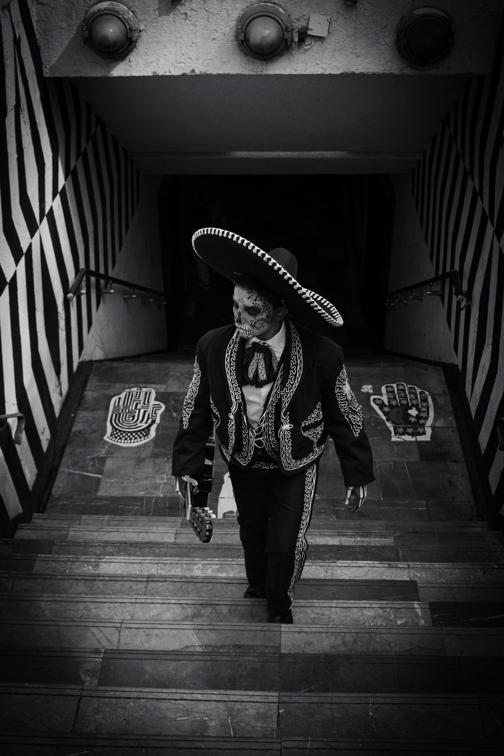 Mariachi performer with skull makeup descends stairs in festive attire.
