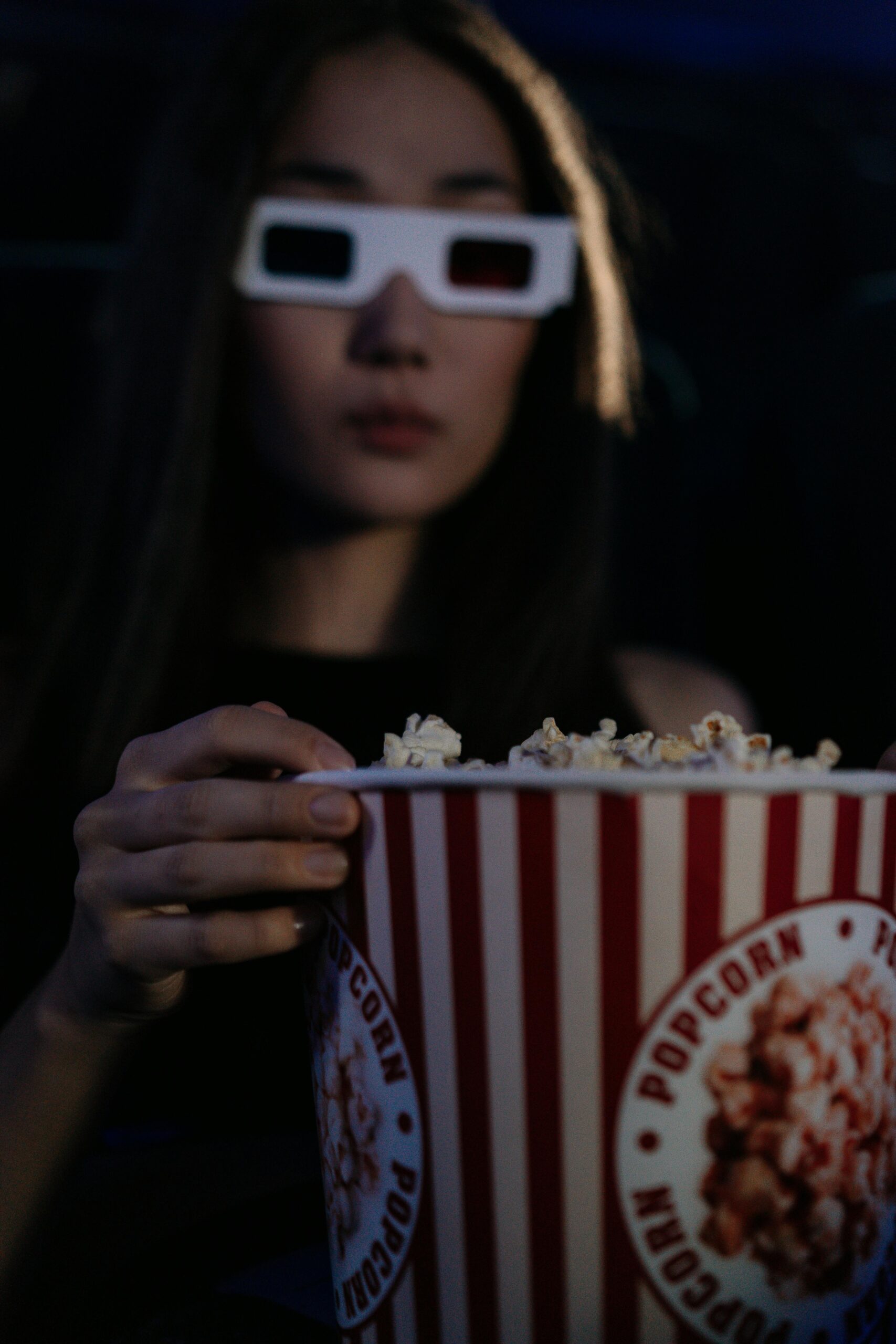 Young woman enjoying movie with 3D glasses and popcorn in a theater setting.