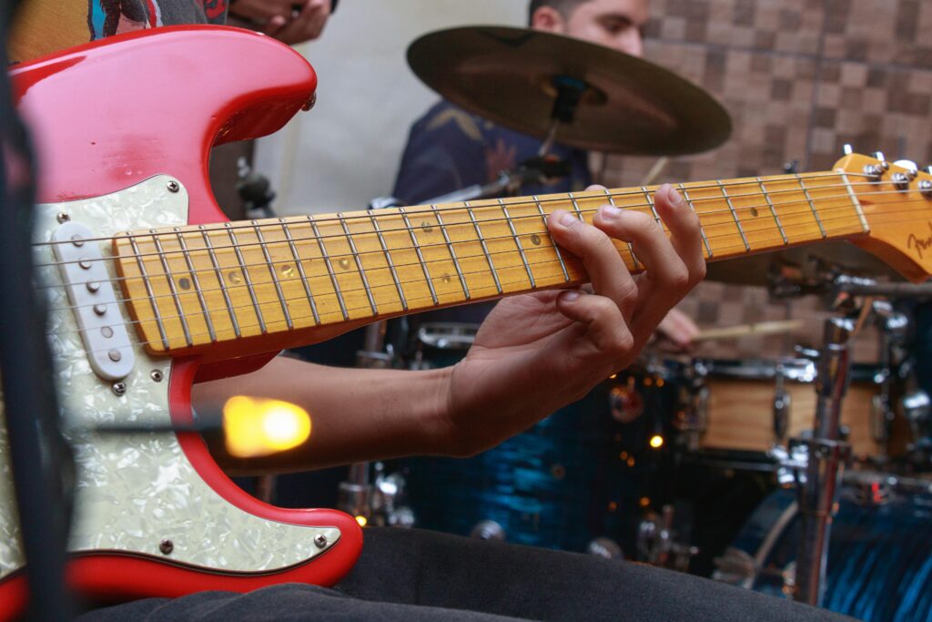 Musician playing guitar in a dynamic band rehearsal setting.